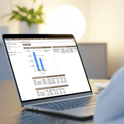 A person uses a laptop displaying financial data and bar charts on the screen, showcasing the power of ExtendAg, with a blurred plant and lamp in the background.