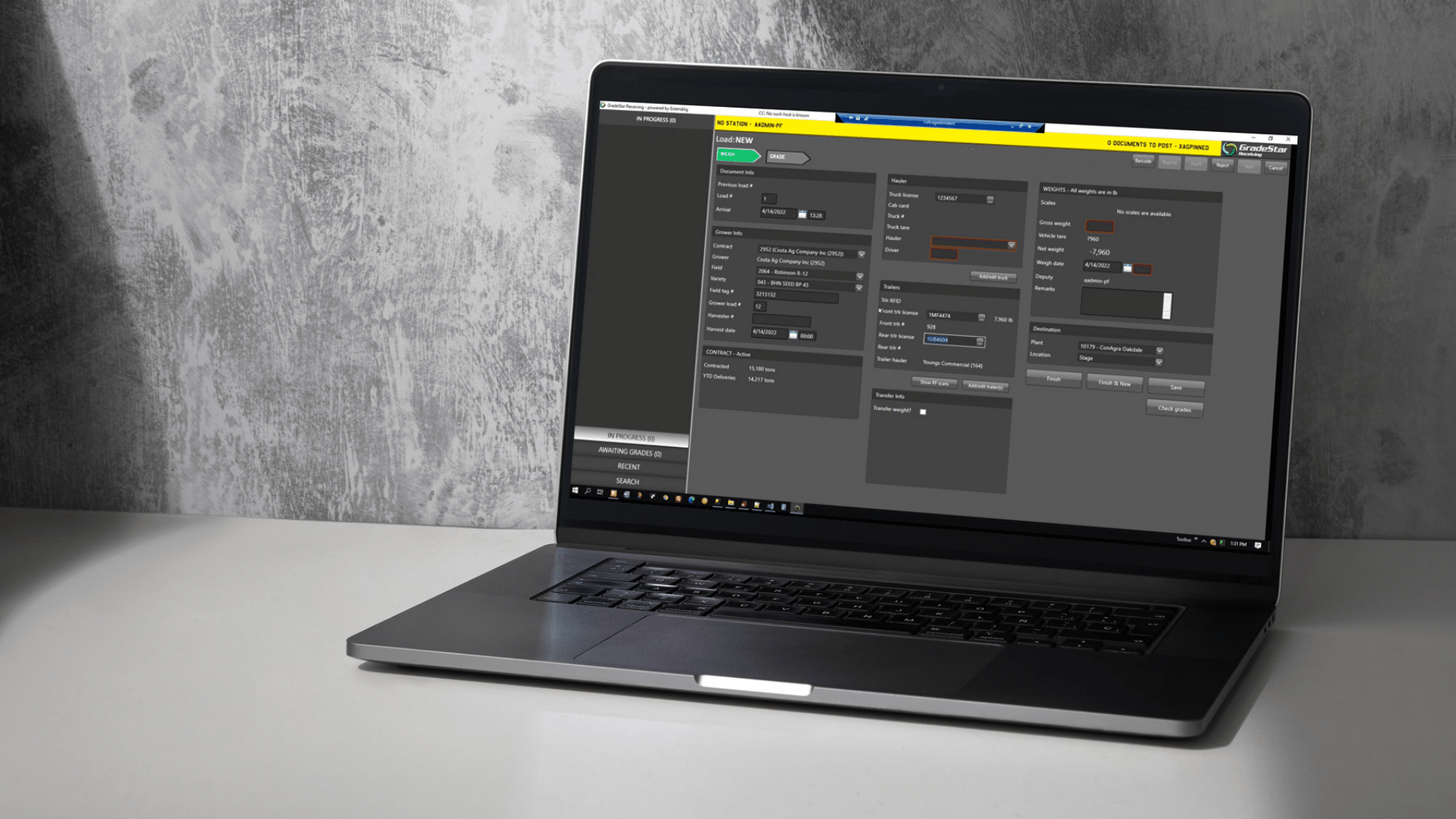 A laptop on a white desk displays the Gradestar software application, showcasing various control panels and input fields on its screen, set against a textured gray wall.