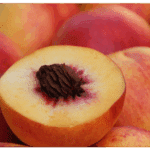 A close-up of a halved peach showing the pit, with whole peaches in the background hints at peach processing. A small white leaf icon is in the bottom right corner.